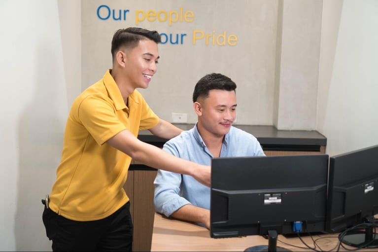 Two male Select VoiceCom employees are engaging in a discussion at the company's call center in the Philippines.