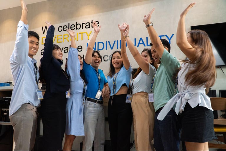 A group of Select VoiceCom employees raising their hands in a photo op in a Philippine call centre office.