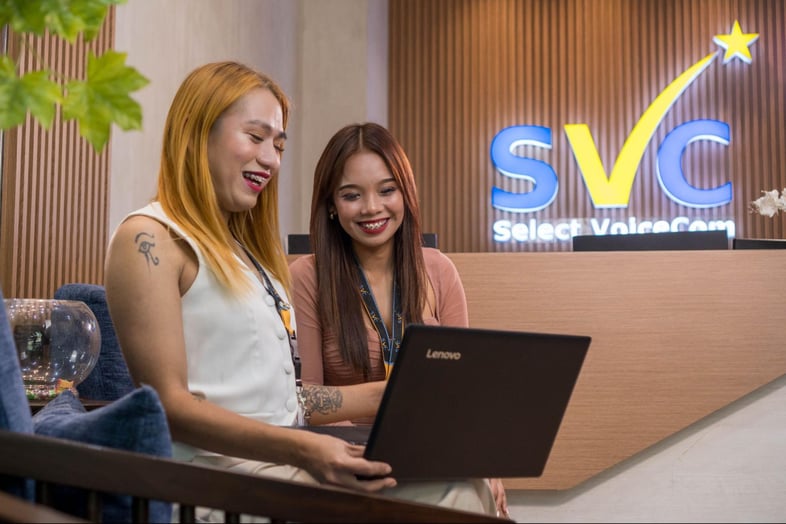 Two female call center agents from Select VoiceCom having a discussion in the office.